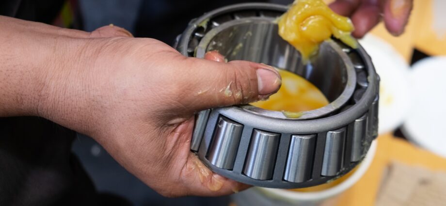 A mechanic in an automotive facility applying a dab of lithium grease to a metal component with their finger.