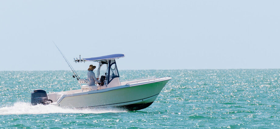 A small fishing boat with an outboard motor and hardtop motoring through turquoise ocean waters on a clear, sunny day.
