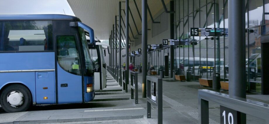 The exterior of a large bus station with buses parked in front of the terminals. The terminals are empty.