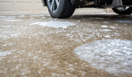 A close-up of a concrete driveway with a car parked on it. The driveway is covered in patches of ice.