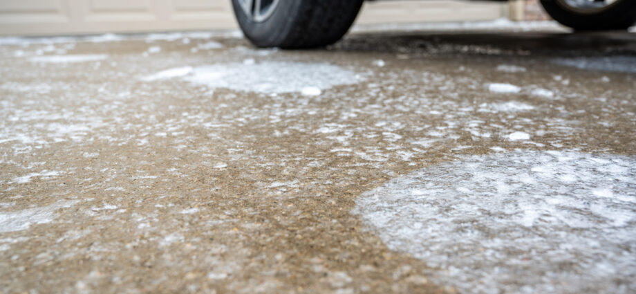 A close-up of a concrete driveway with a car parked on it. The driveway is covered in patches of ice.