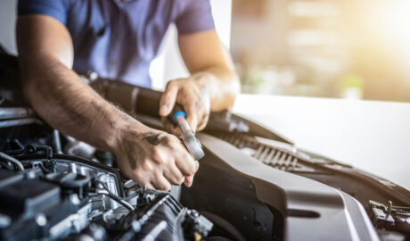 Close-up of a man's hands as he works on his car's engine with a wrench as a project. He is wearing a purple shirt.