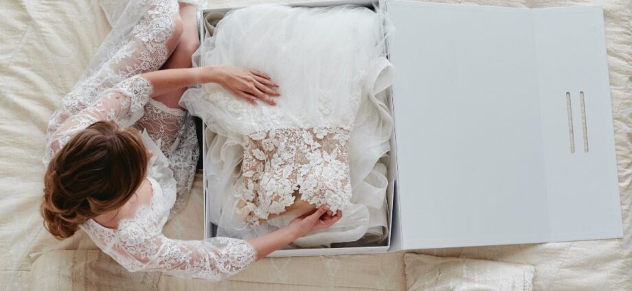 5 Creative Things You Can Do With Your Wedding Dress After the Ceremony 1 A woman sits on her bed as she opens up the box that holds her beautiful wedding dress, covered in tulle and lace.