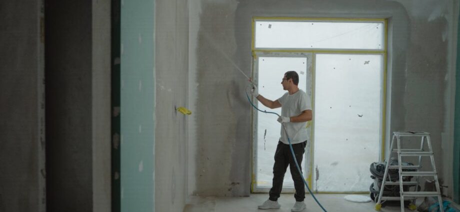 A man in a white shirt holding a spray paint hose doing a home remodel paint job.