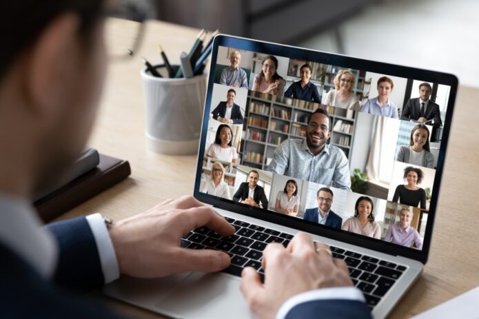 How to Keep Remote Workers Engaged in the Company 6 A person in a suit sitting in front of a laptop. The laptop's screen shows several other people on a video call.