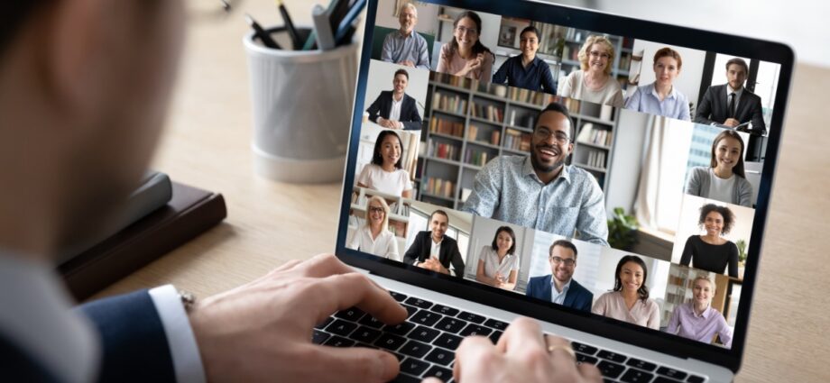 A person in a suit sitting in front of a laptop. The laptop's screen shows several other people on a video call.