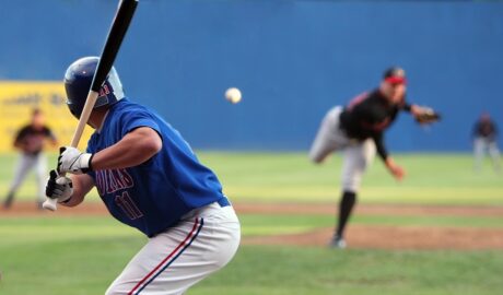 A baseball batter in a blue uniform prepares to swing as the pitcher releases the ball during a live game on the field.