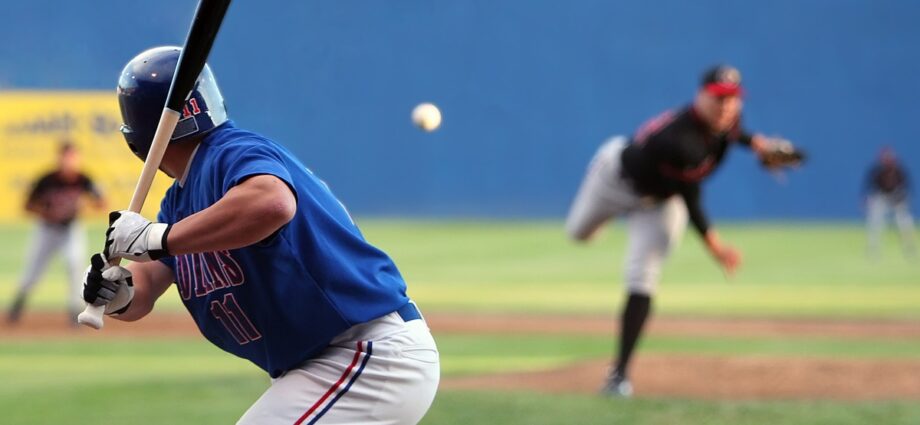 A baseball batter in a blue uniform prepares to swing as the pitcher releases the ball during a live game on the field.