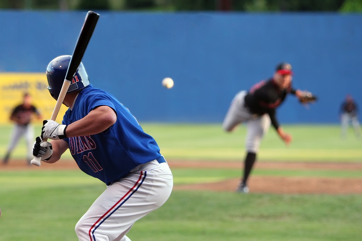 A baseball batter in a blue uniform prepares to swing as the pitcher releases the ball during a live game on the field.