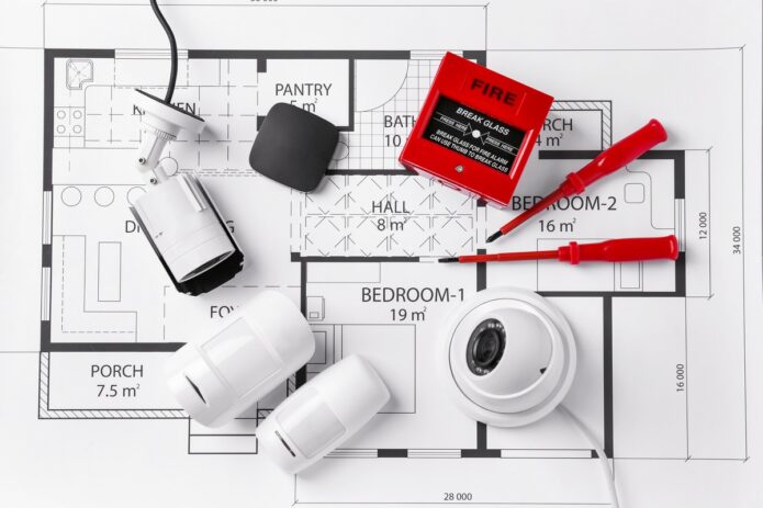 A collection of home safety and monitoring equipment all sitting on top of a blueprint for a small home.
