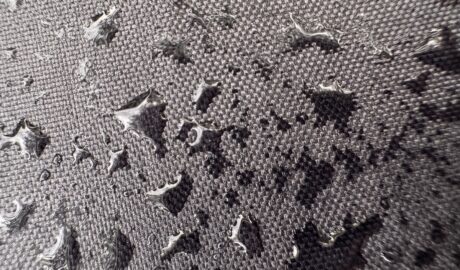Close-up of water drops scattered across textured gray fabric, with shiny beads resting on the woven surface.