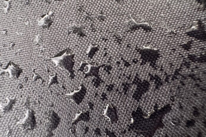 Close-up of water drops scattered across textured gray fabric, with shiny beads resting on the woven surface.