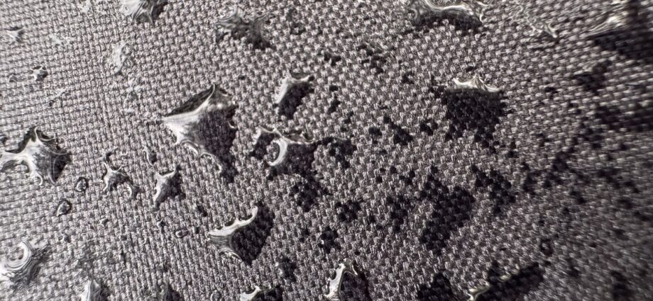 Why Some Surfaces Stay Dry Even in Heavy Rain 1 Close-up of water drops scattered across textured gray fabric, with shiny beads resting on the woven surface.