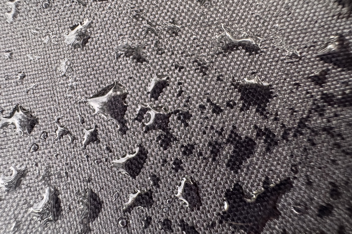 Close-up of water drops scattered across textured gray fabric, with shiny beads resting on the woven surface.