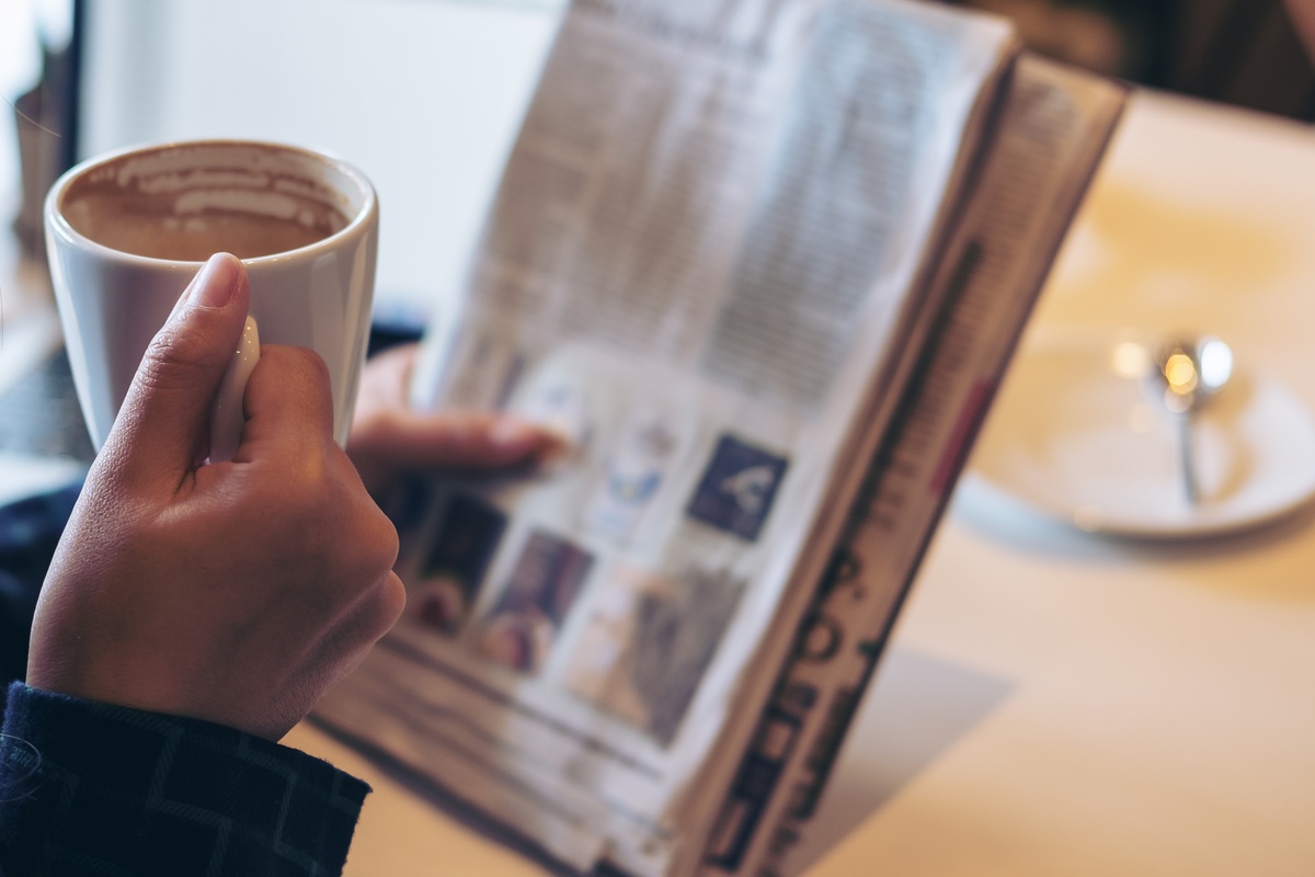Calmer Coffee Choices for Busy Morning Routines 23 Someone reads the paper with their left hand and drinks out of a hot coffee mug with their right hand.