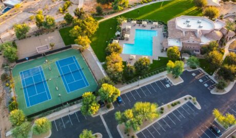 An aerial scene of a community center with tennis courts, a swimming pool, trees, lawns, and parking areas.