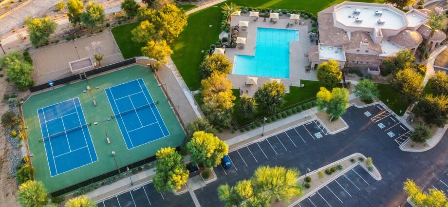 An aerial scene of a community center with tennis courts, a swimming pool, trees, lawns, and parking areas.
