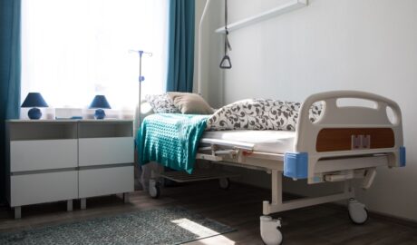 A hospital bed tucked away into the corner of a bedroom. The bed has a floral comforter and a blue knit blanket.