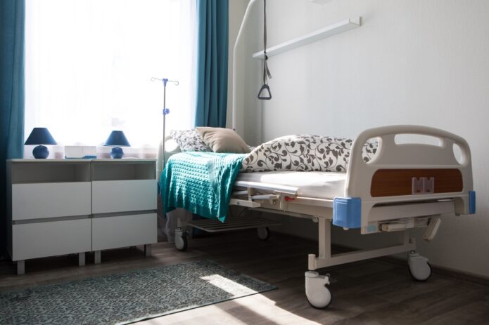 The Practical Side of Hospital Beds at Home 1 A hospital bed tucked away into the corner of a bedroom. The bed has a floral comforter and a blue knit blanket.
