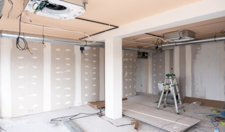 A large room in the middle of being renovated. There is finished drywall and an HVAC system visible.