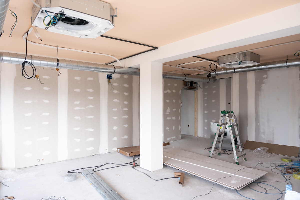 A large room in the middle of being renovated. There is finished drywall and an HVAC system visible.